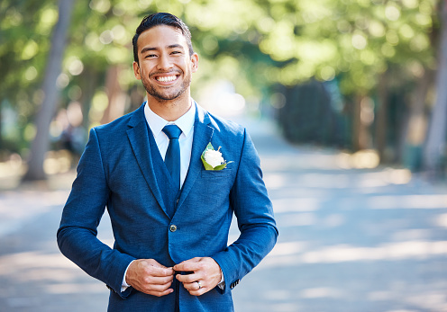 Handsome groom wearing a blue suit with a white shirt and tie. Bridegroom fastening his jacket while standing outdoors on a sunny day