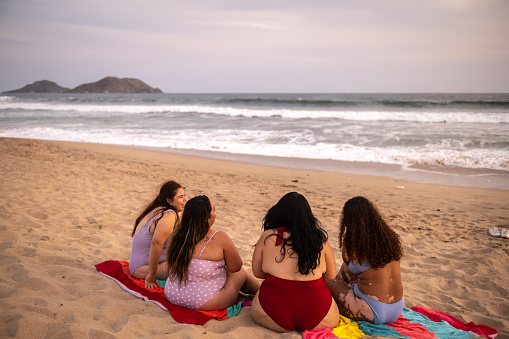 Female friends sitting on the sand and talking on the beach