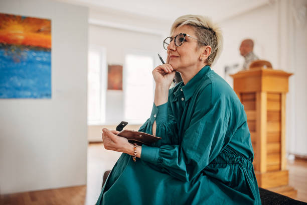 Woman in art gallery Diverse visitors in modern art gallery, woman sitting, taking notes and looking at paintings. gallery opening stock pictures, royalty-free photos & images