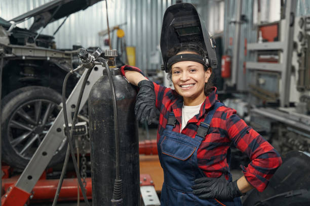 Cheerful woman auto mechanic standing in vehicle repair shop Woman car service technician looking at cameras and smiling while standing by gas cylinder at repair service station welder stock pictures, royalty-free photos & images