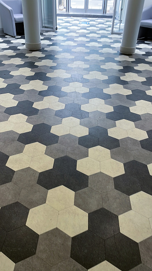 Stock photo showing an expanse of hallway floor covered with tessellating black, white and grey hexagonal tiles.