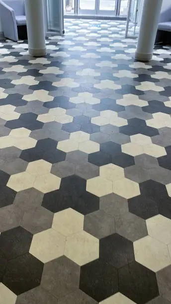 Photo of Image of tessellating black, white and grey hexagonal tiles covering expanse of hallway floor, elevated view, focus on foreground