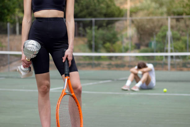 weibliche gewinnerin des tennisturniers mit pokal in der hand vorne und lockererem mann im hintergrund unscharf - winner looser stock-fotos und bilder