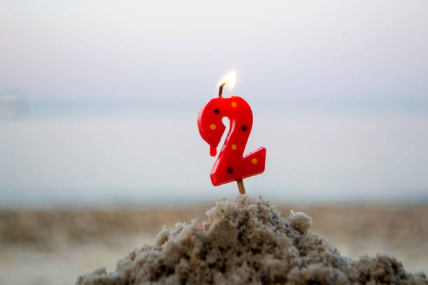 istock Candle number two on stick inserted into sand and burns. Lighted candle 1399005670