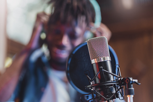 condenser microphone with antipop in front of the blurred face of an African guy singing or talking live - technology concept of young people creating contents and casting online