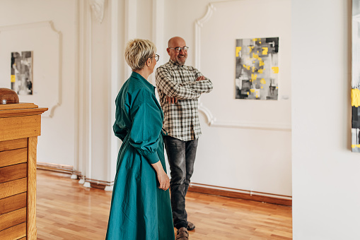 Mature man and woman in modern art gallery looking at paintings.