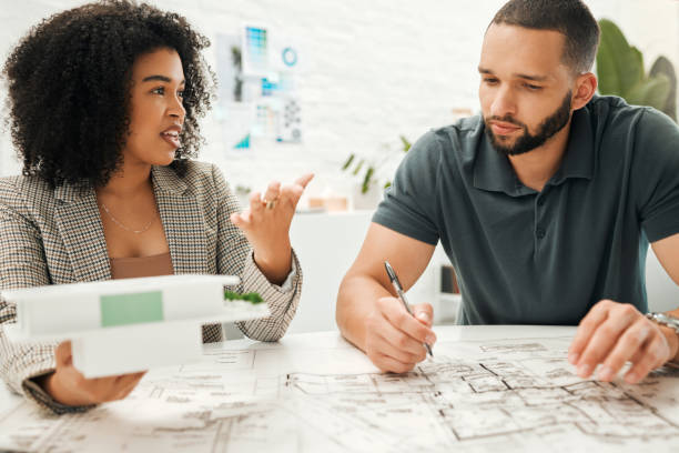 istock Two architectural coworkers planning a building project. Young designers working on a blueprint. Businesspeople collaborate on a building project. Professional designers working together on a 3D model 1399012317