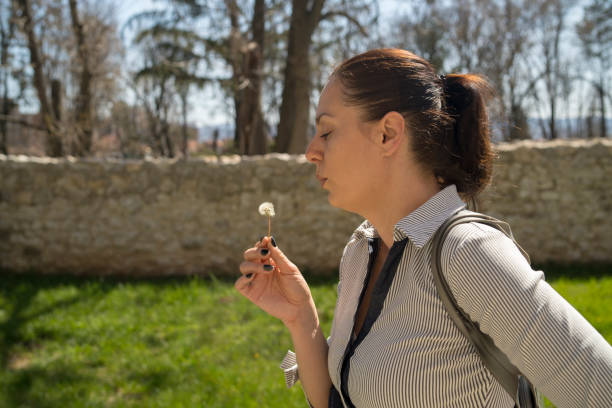Beautiful Young Woman sitting on the field in green grass and blowing dandelion.