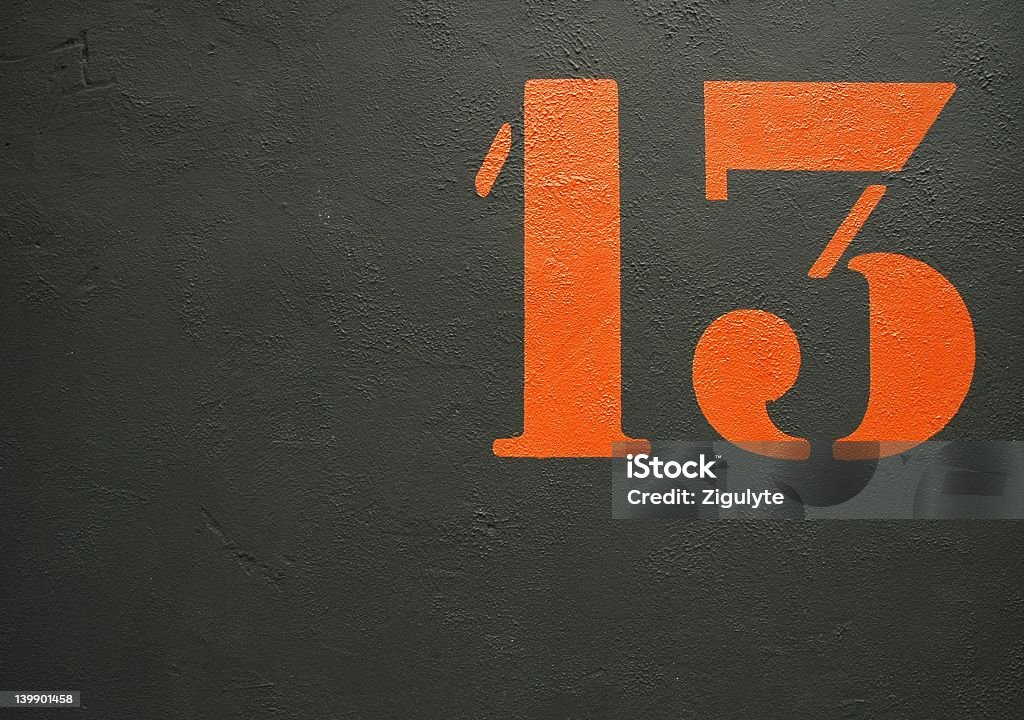 An orange stenciled number 13 on a black background on the wall Number 13 Stock Photo