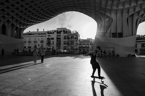 Seville, Spain, April 9, 2022: City life under the Metropol Parasol during a sunny and warm spring day on April 9, 2022 in Seville, Spain. People enjoy the shadow and freshness under the Metropol Parasol architecture. Young guys skating at sunset.