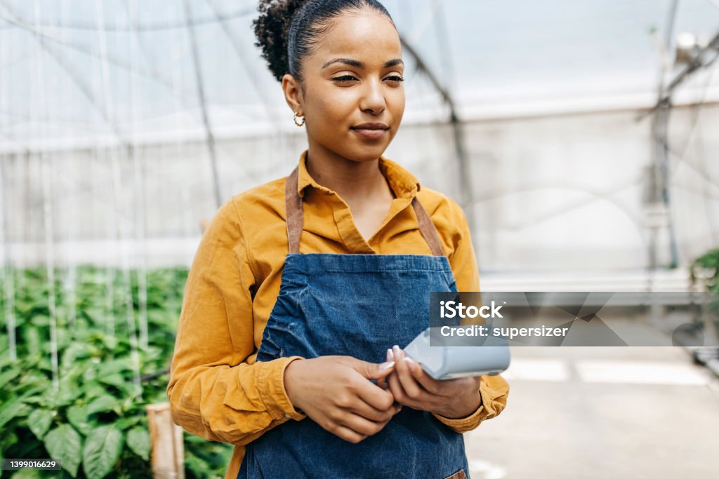 Woman holding card reader int he greenhouse Portrait of the latin woman wearing apron and holding wireless credit card reader Credit Card Reader Stock Photo