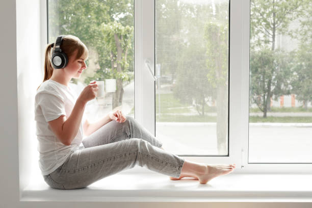 une femme écoute de la musique et des boissons dans une tasse sur la fenêtre - fresh coffee audio photos et images de collection
