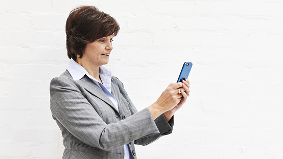 A businesswoman using a phone, isolated on a white background. A mature female executive browsing online for business with her smartphone in an office or studio