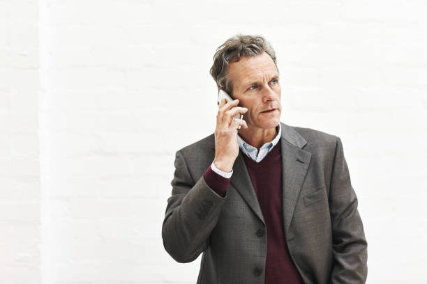 a businessman using a phone to make a call, isolated on a white background. a mature male executive talking on a smartphone for business in an office or studio - isolated businessman sadness business person imagens e fotografias de stock