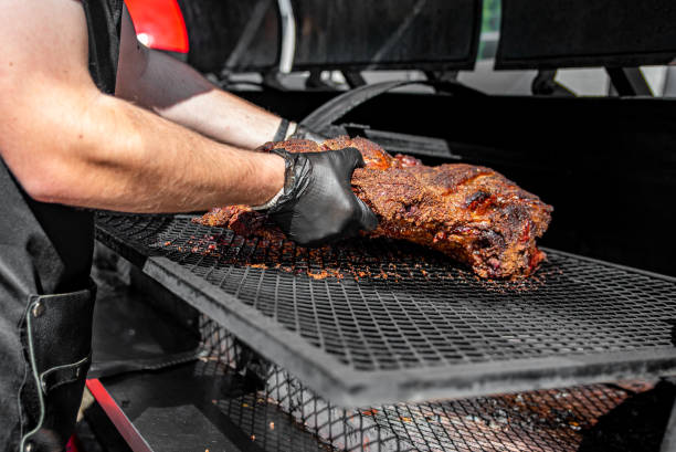 chef cuisinier à la main de la viande de bœuf grillée dans un fumoir bbq. - aliment fumé photos et images de collection