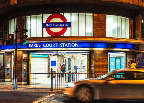 London, UK - A car on the street passing Earl's Court London Underground station at night.