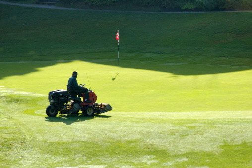 A golf course worker mows the grass of a green, in the early morning.