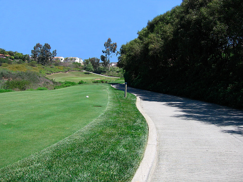 A winding cement path for golf carts next to a tee for a golf hole.