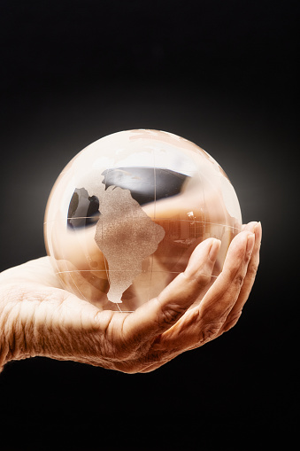 Senior woman's aged hand supports a crystal ball world globe.