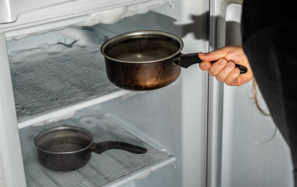 Melt ice with hot water. Melting the ice from the freezer with the help of saucepans with hot water. fridge defrost stock pictures, royalty-free photos & images