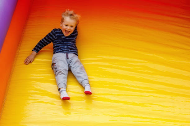 A hilarious little boy slides down at a high speed off a large, bright yellow trampoline. Child on the move, there is free space for text in the photo stock photo