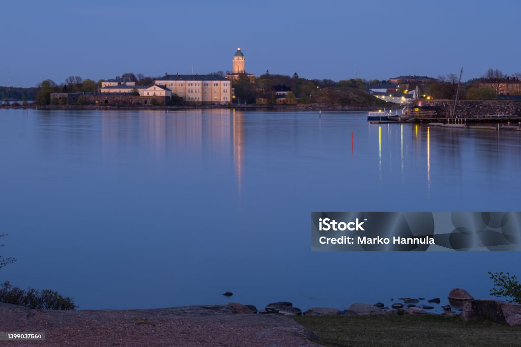 Suomenlinna fortress across the river. A lighthouse casting reflections on the calm sea. Helsinki / Finland - MAY 22, 2022: Suomenlinna fortress across the river. A lighthouse casting reflections on the calm sea. Archipelago Stock Photo