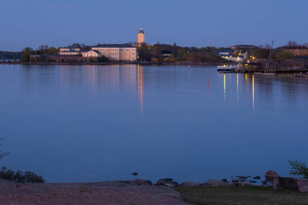 Suomenlinna fortress across the river. A lighthouse casting reflections on the calm sea. stock photo