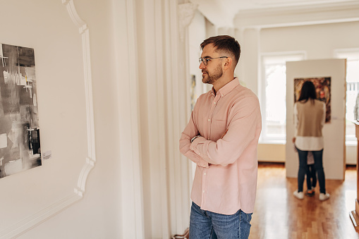 Handsome man in modern art gallery looking at paintings.