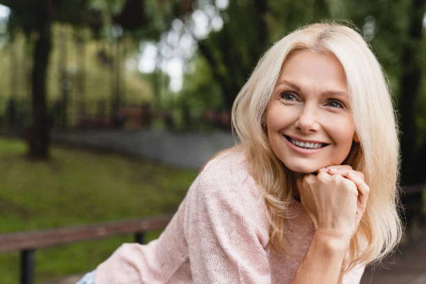 cheerful caucasian mature blonde woman wife with toothy smile relaxing resting walking in city park forest alone outdoors - footpath field nature contemplation imagens e fotografias de stock