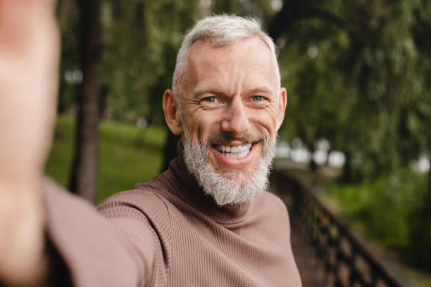 istock Smiling caucasian mature man looking at the camera, taking selfie on smart phone, having video call, vlogging blogging outdoors in park. 1399041993