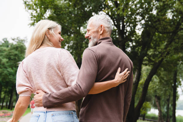 esposa y esposo caucásico maduro uniéndose mientras caminan juntos en el parque en una cita. concepto de relación románica. toma de vista trasera - senior adult mature adult senior couple heterosexual couple fotografías e imágenes de stock