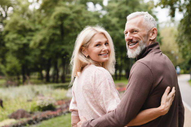 sonrientes felices cónyuges caucásicos maduros abrazándose mientras caminan juntos en una cita en el parque. vinculación, amor y relación - senior adult mature adult senior couple heterosexual couple fotografías e imágenes de stock