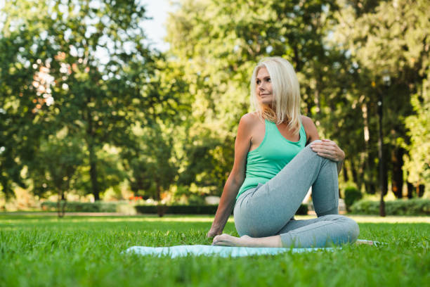 mature fit woman stretching her body on fitness mat, doing workout in park, practicing breathing exercises. active healthy lifestyle. - women yoga yoga class mature adult imagens e fotografias de stock