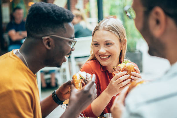 Friends and fast food Friends eating burgers and have fun in outdoor restaurant bacon cheeseburger stock pictures, royalty-free photos & images