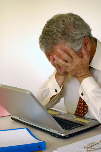 A businessman holds his head in his hands in front of his laptop computer, in despair. Space for text on the white background.
