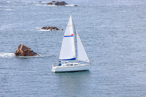 A scenic view of a sailboat along the rocky Moray Scottish coast on a calm sea