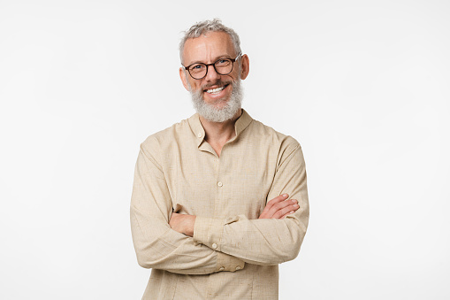 Inteligente hombre independiente de mediana edad maduro caucásico con camisa beige con gafas mirando a la cámara con los brazos cruzados aislados en fondo blanco photo