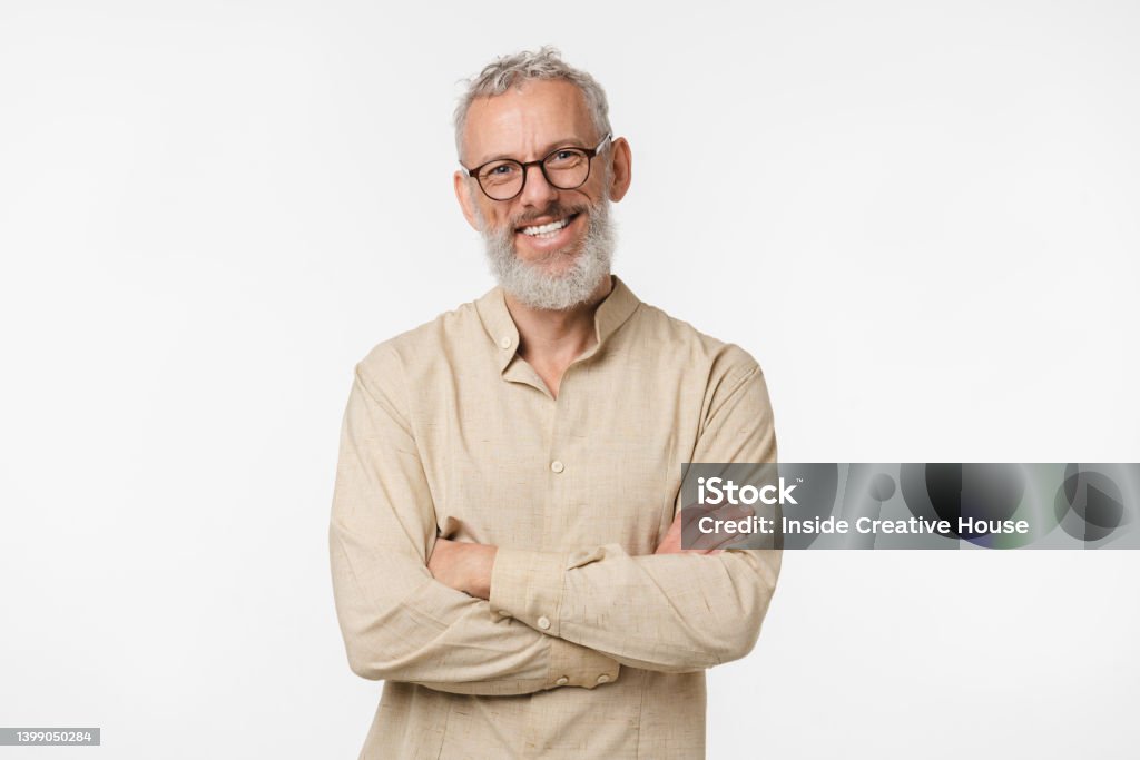Smart caucasian mature middle-aged freelancer man in beige shirt wearing glasses looking at camera with arms crossed isolated in white background Men Stock Photo