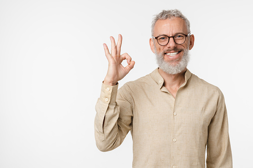 Positive happy caucasian mature middle-aged man smiling with toothy smile wearing glasses showing okay gesture isolated in white background