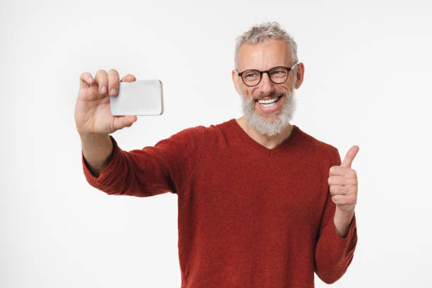 istock Cheerful caucasian grey-haired mature man freelancer using smart phone cellphone for videocall conversation online, vlogging, blogging, taking selfie isolated in white background 1399052079
