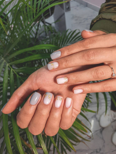 istock Women's hands with gray-beige manicure and gold design. Beautiful nails covered with gradient gel polish in gray and beige with gold spotted sequins. 1399056132