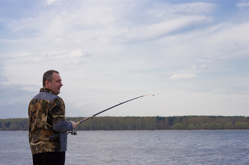 A man is fishing with a fishing rod. A man on the riverbank is fishing. A man holds a fishing rod in his hands