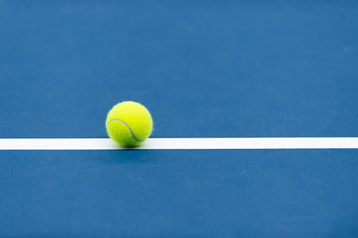 Yellow tennis ball with white line on blue court. Horizontal sport theme poster, greeting cards\