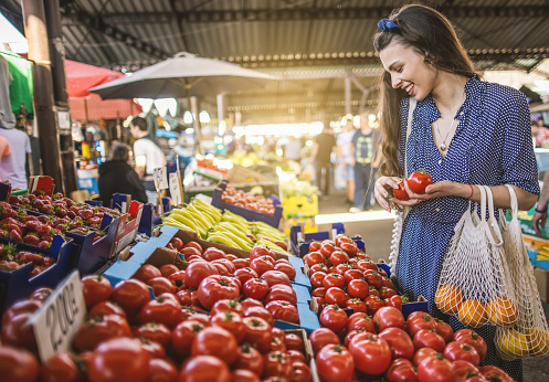 Photo of smiling  young woman buying fresh tomatoes at the market