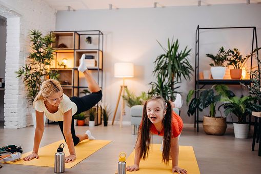 Young mother and cute daughter with down syndrome working out at home together