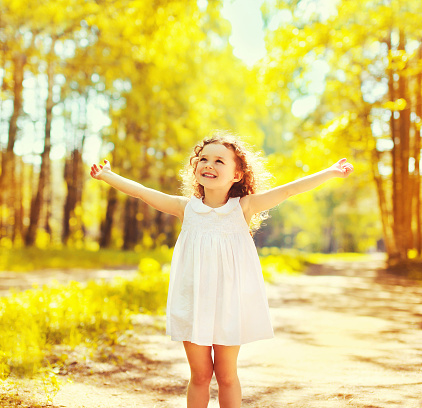 Happy little girl child having fun raising her hands up in sunny summer day