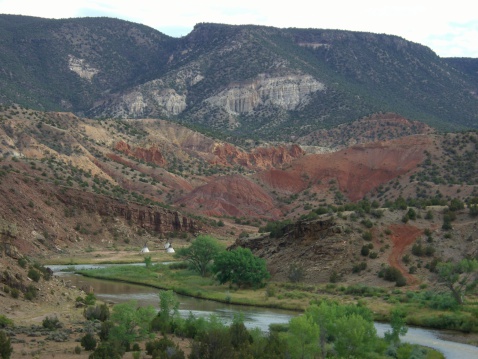 Photo of the Chama river in New Mexico and mountains.  An indian village can be seen at the base of the mountains.