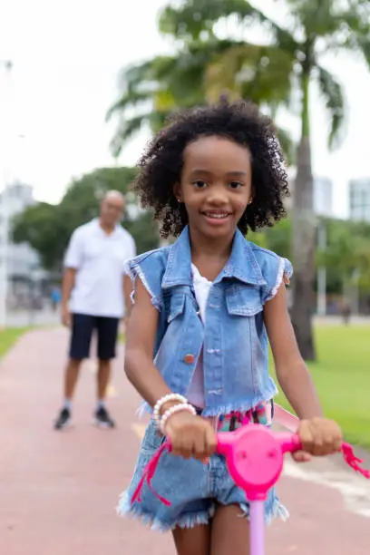 A portrait of a little girl with her afro hair playing on a scooter in the park