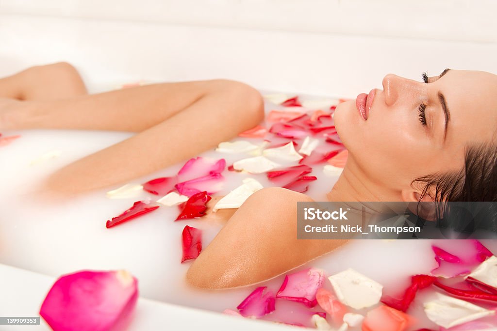 Linda garota nua desfruta de um banho com pétalas de leite e - Foto de stock de Adulto royalty-free