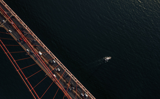 Overhead drone view of modern suspension bridge with riding automobiles over calm rippling river in Lisbon